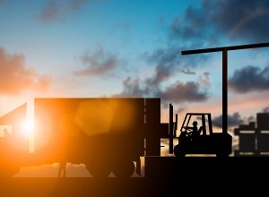 Silhouette Forklift truck lifting cargo container on a truck in the warehouse during sunset.