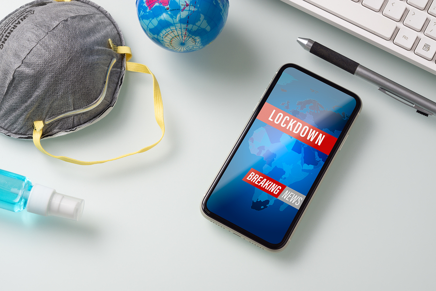 COVID-19 lockdown shown on cell phone next to keyboard and face mask