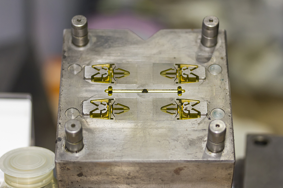 A close-up picture of a multi-cavity plastic injection mold with four similar parts inside, meant to serve as a comparison between multi-cavity molds and family molds