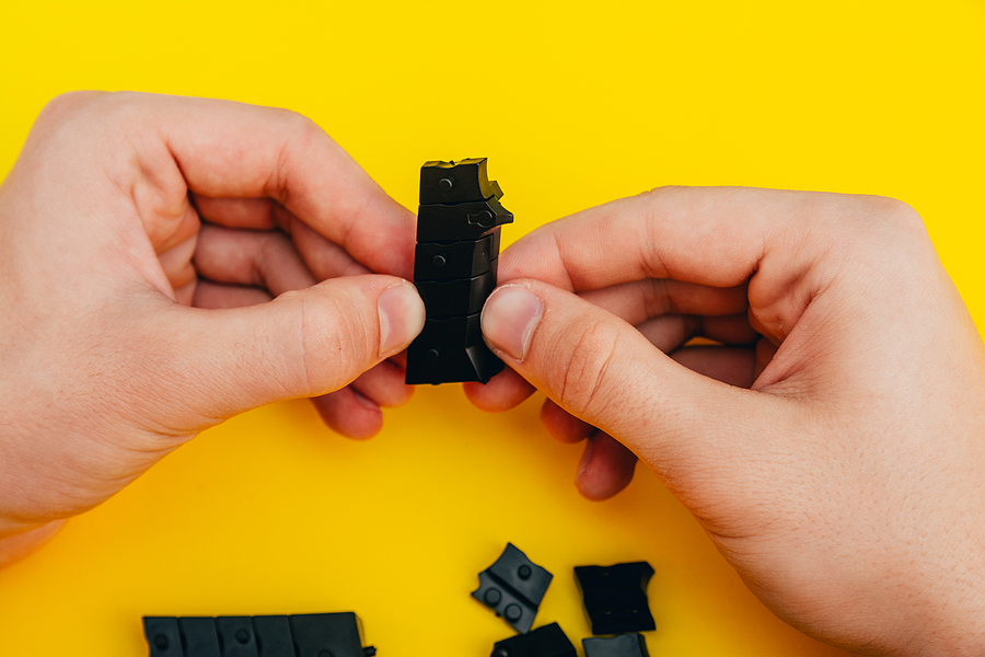 Hands holding a black prototype part for toy on a yellow background, inidcating a part make with rapid part prototyping