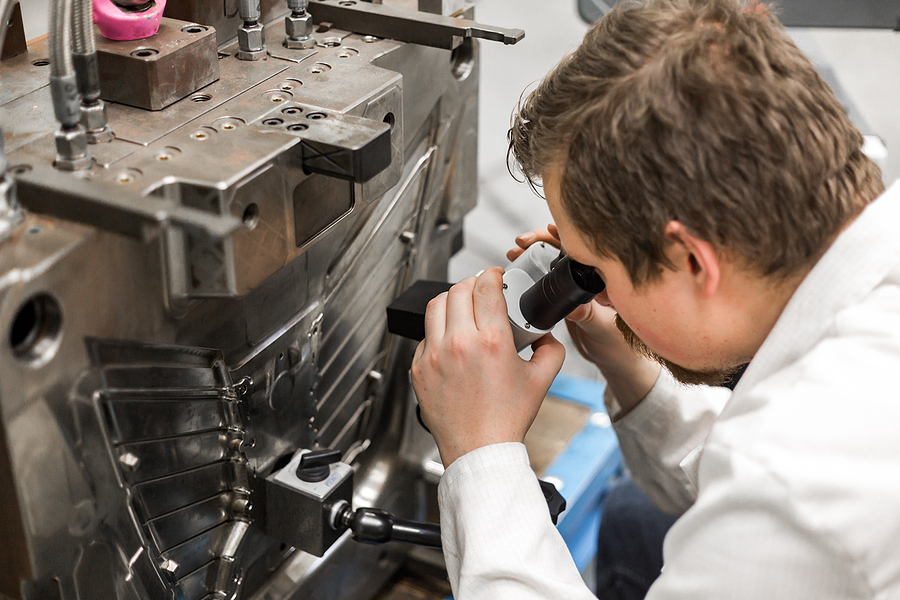 A quality control engineer looking for part deficiencies by using a microscope next to a injection molding machine