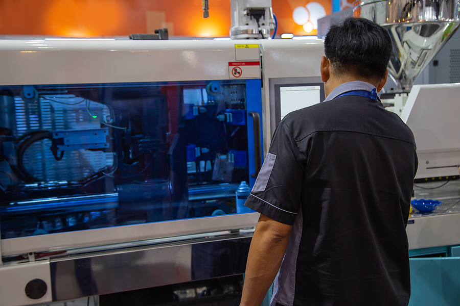 A male worker operating an industrial plastic injection molding machine at a turnkey manufacturer