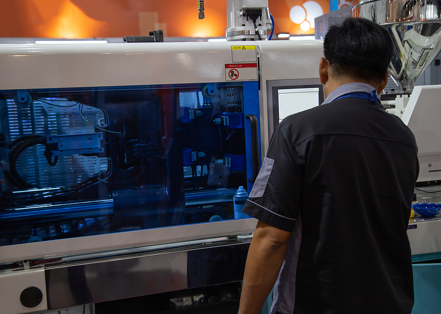 A worker operating an industrial plastic injection molding machine.