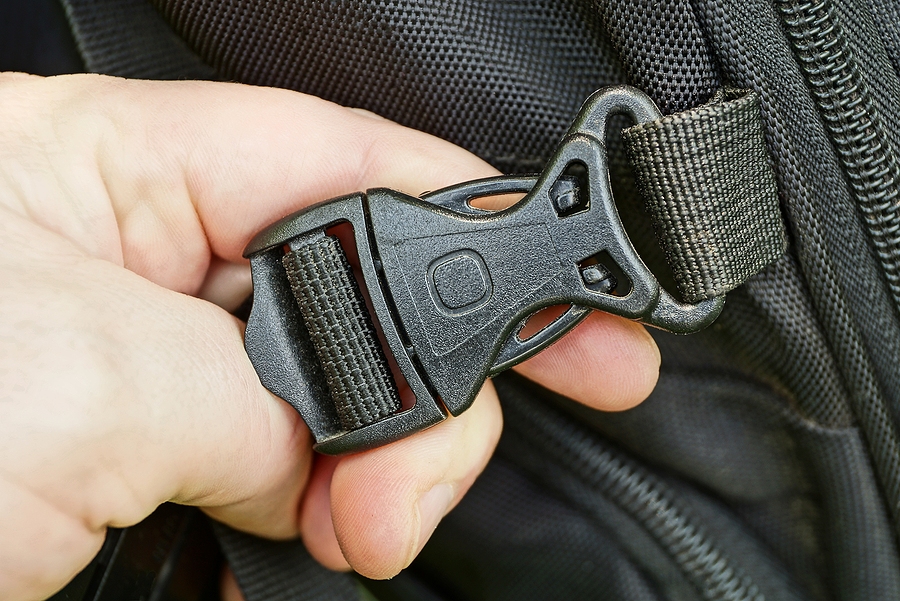 A hand holding the snap and latch part of a black backpack, an example of an undercut used in plastic injection molding.