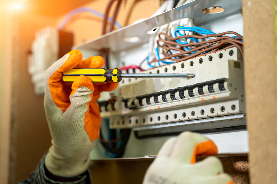 A gloved hand holding a screw driver next to plastic electrical housing make with engineering-grade resins. 