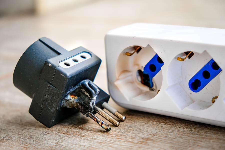 A three-pronged plug surrounded in burnt plastic laying next to a power strip with burnt plastic.