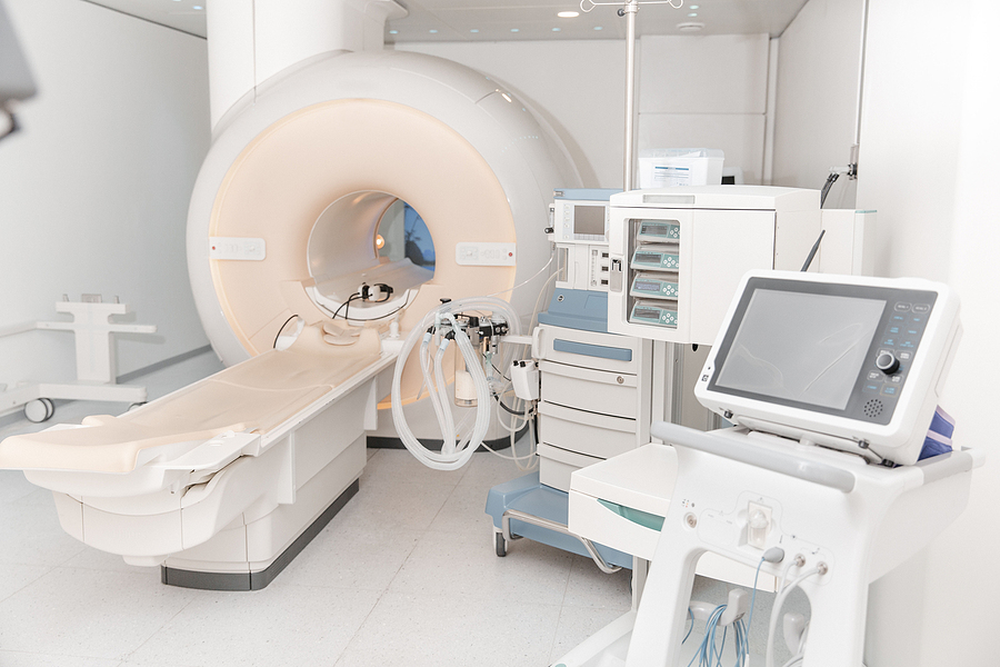 A hospital room with an MRI machine and several other machines composed of white plastics.