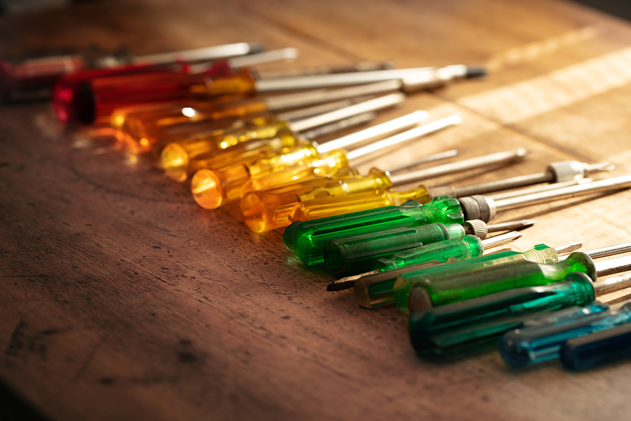 Multiple screw drivers lined up on a wooden table with the color scheme of a rainbow, meant to display multi-material plastic injection molding.