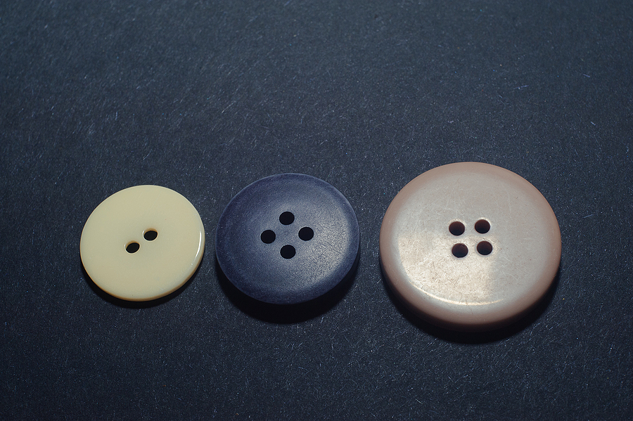 Tan, black, and brown clothes buttons lined in a row atop a black surface, when to exhibit the history behind plastic injection molding.
