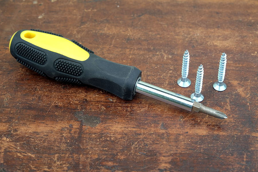 A screwdriver created via insert molding with a black and yellow handle next to screws on a wooden table.