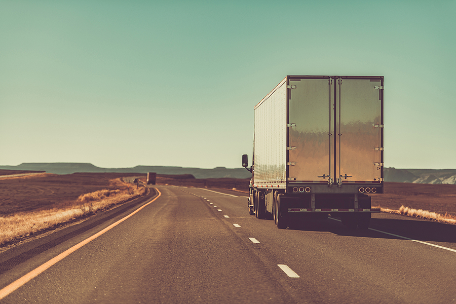 A rear view of a semi-trailer truck traveling on an interstate in the desert, meant to depict the benefits of injection molding on the transportation industry.