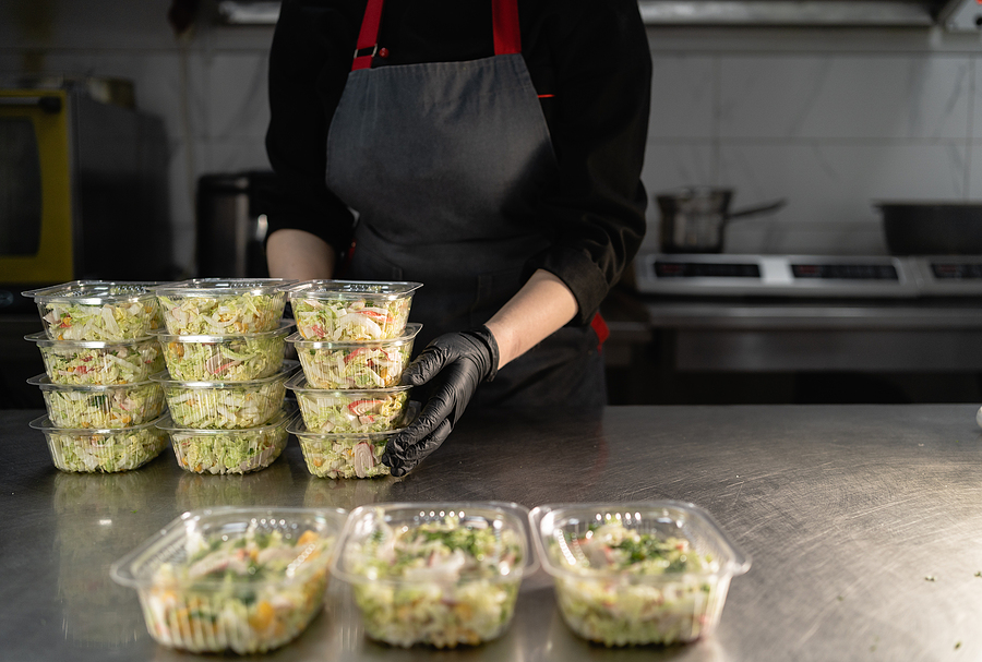 A chef wearing a black apron and black gloves packing food into biopolymer food packaging.