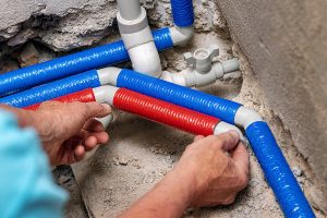 A close-up of a plumbers hands installing red and blue insulated polypropylene pipes.