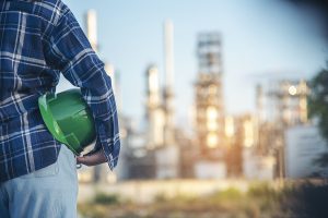 Man standing with green safety helmet in front of manufacturing site.