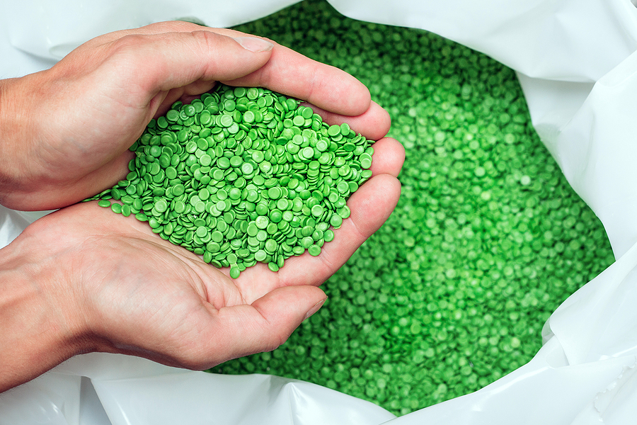 Hands holding green resin pellets above a bag filled with more.